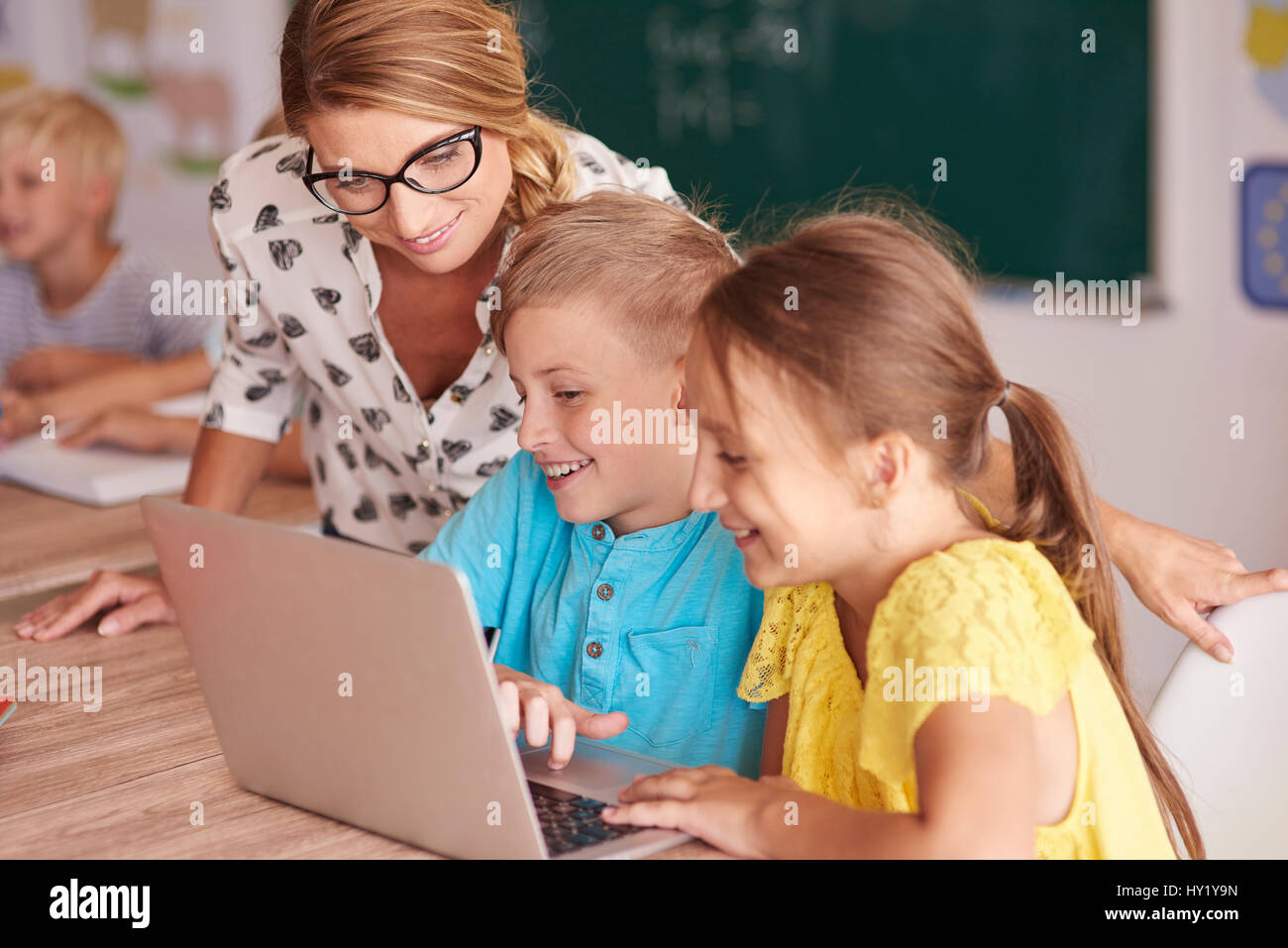 Teacher with students using laptop in classroom Stock Photo