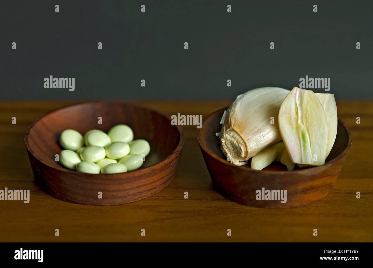 This stock photo shows a close up of Garlic pills and fresh cut Garlic bulbs in small wooden bowls. This image is meant to symbolize the choice betwee Stock Photo