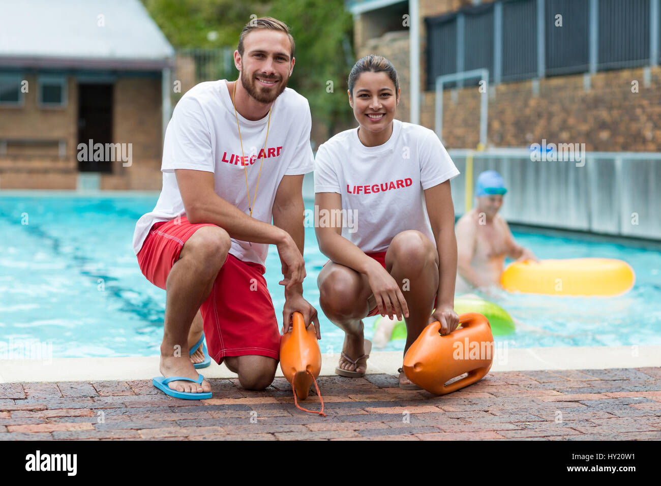 Portrait of male and female lifeguards holding rescue cans at poolside Stock Photo