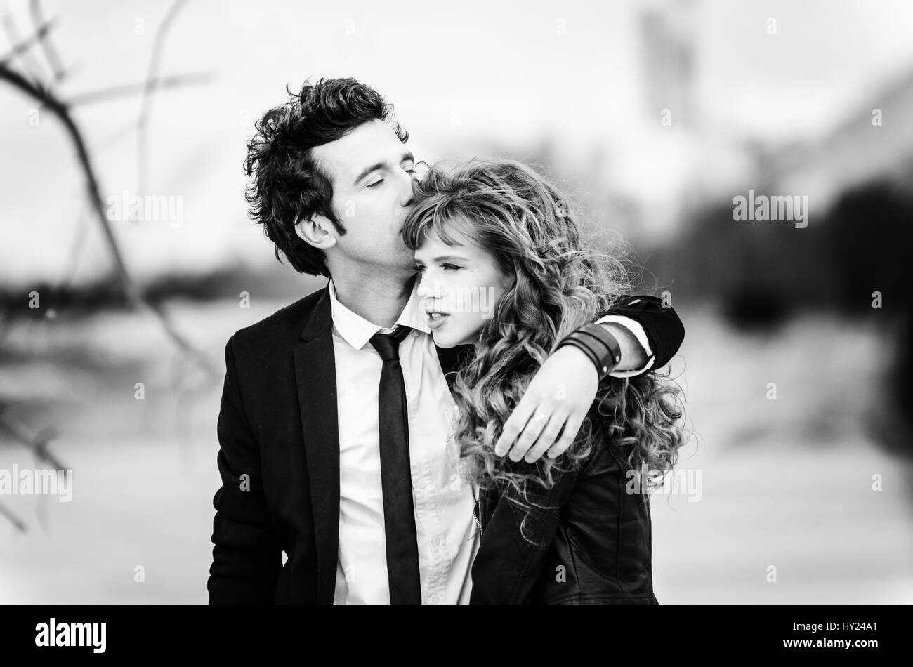 Cute couple embraces. Portrait of stylish young man in suit with tie hugs beautiful girl and kisses. Successful relationship and happy moments concept Stock Photo