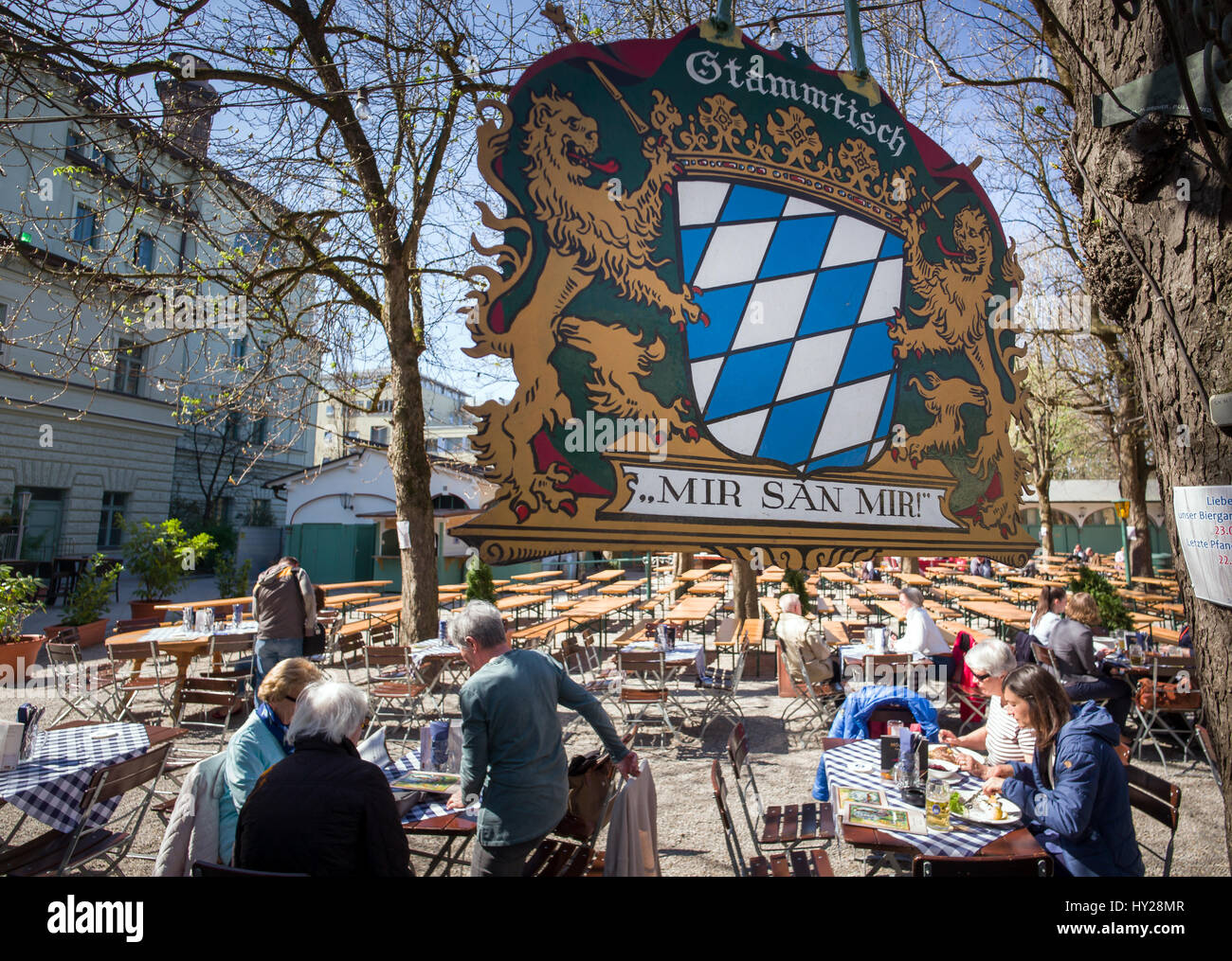A sign with the Bavarian coat of arms and the words 'Stammtisch - Mir san Mir!' ('Regulars' table - We are we are!') hangs over a beer garden in Munich, Germany, 31 March 2017. Photo: Peter Kneffel/dpa Stock Photo