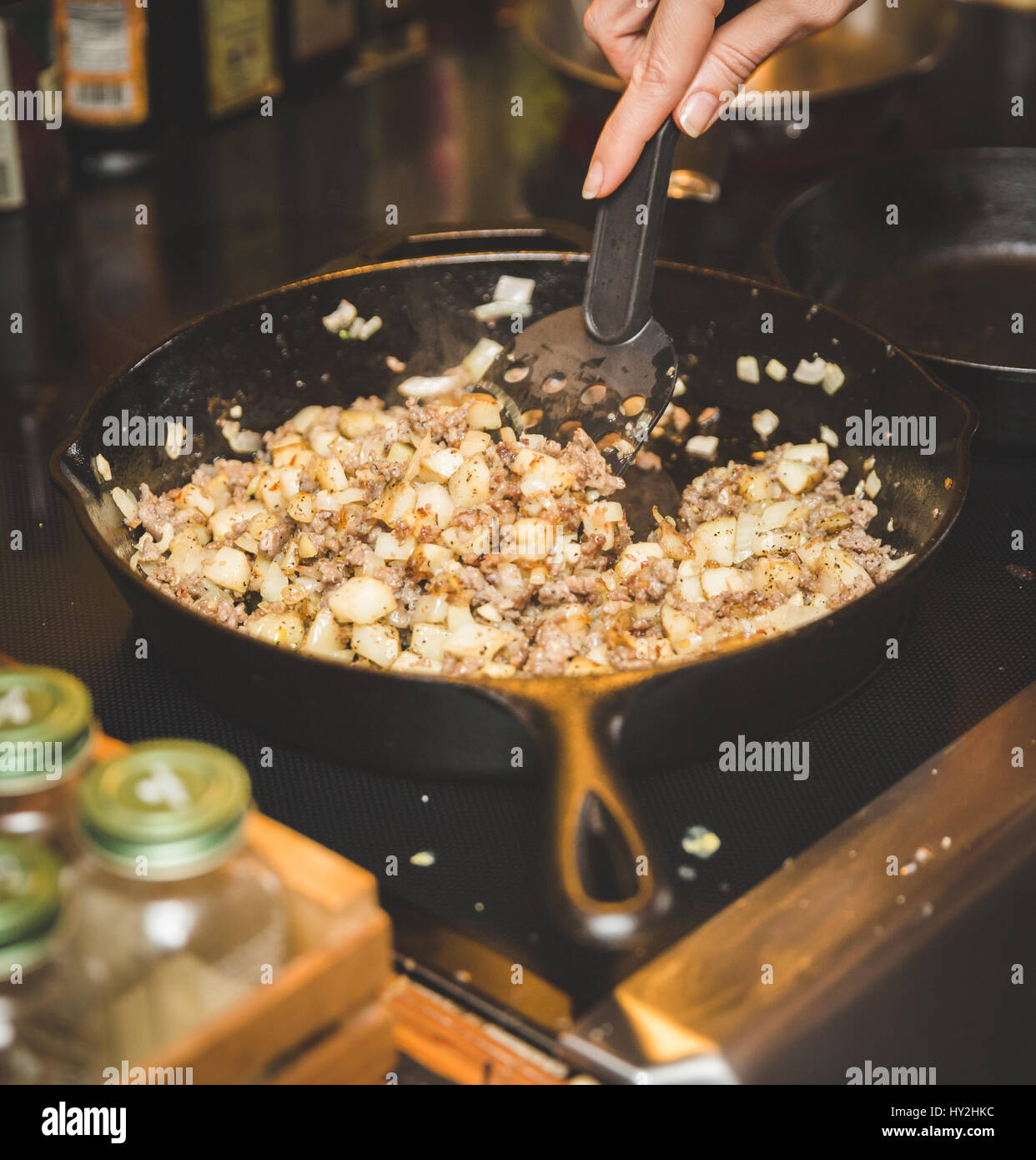 Person cooking sausage, potatoes, onions, and other vegetables in cast