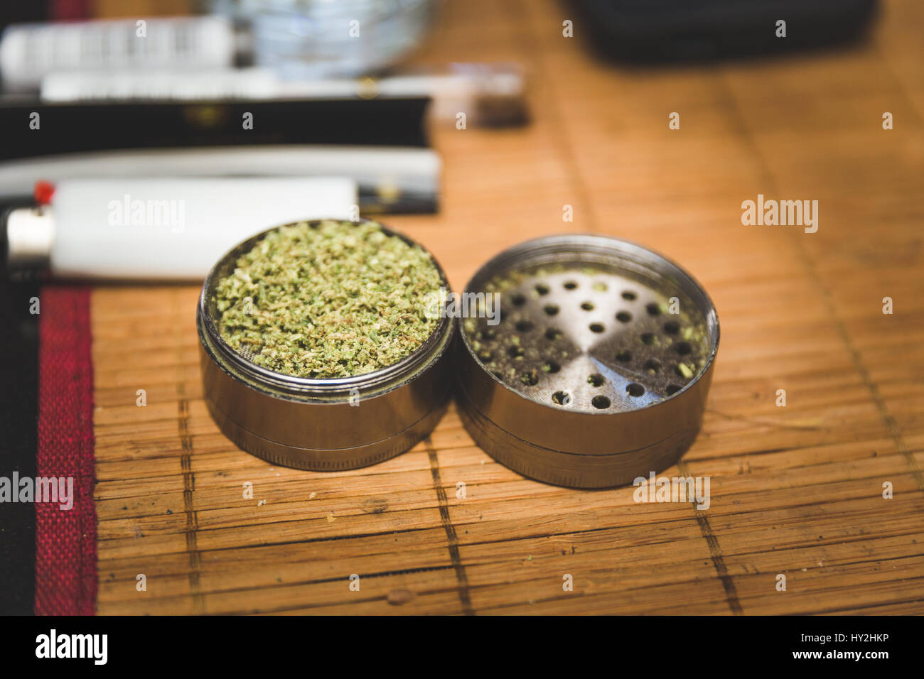 Steel or metal grinder full of freshly ground cannibus flower. Related smoking accessories nearby. Stock Photo