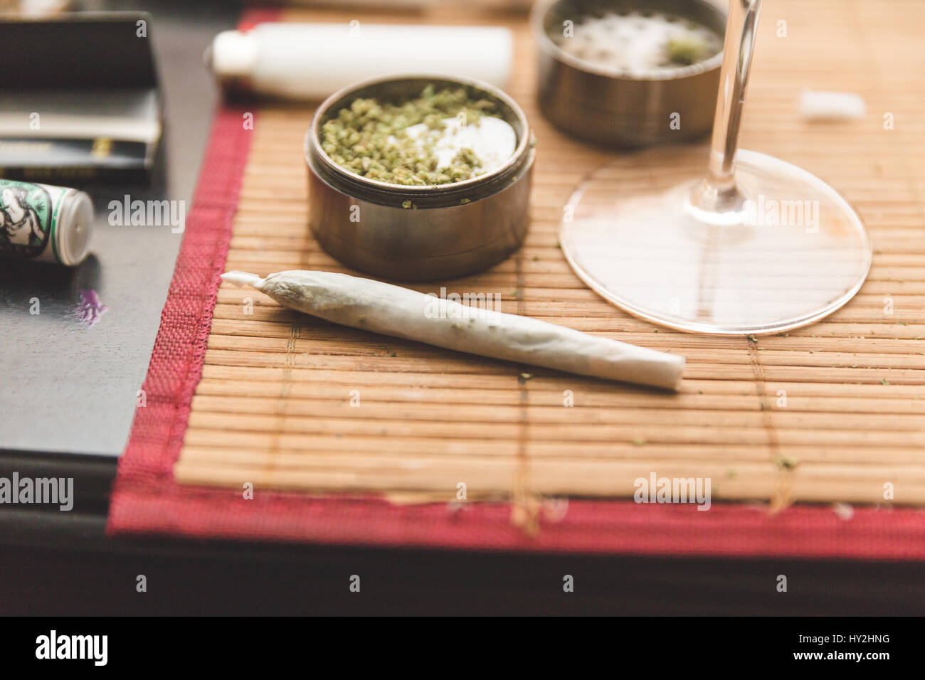 Joint, grinder, cannabis buds, and related items on a table. Stock Photo