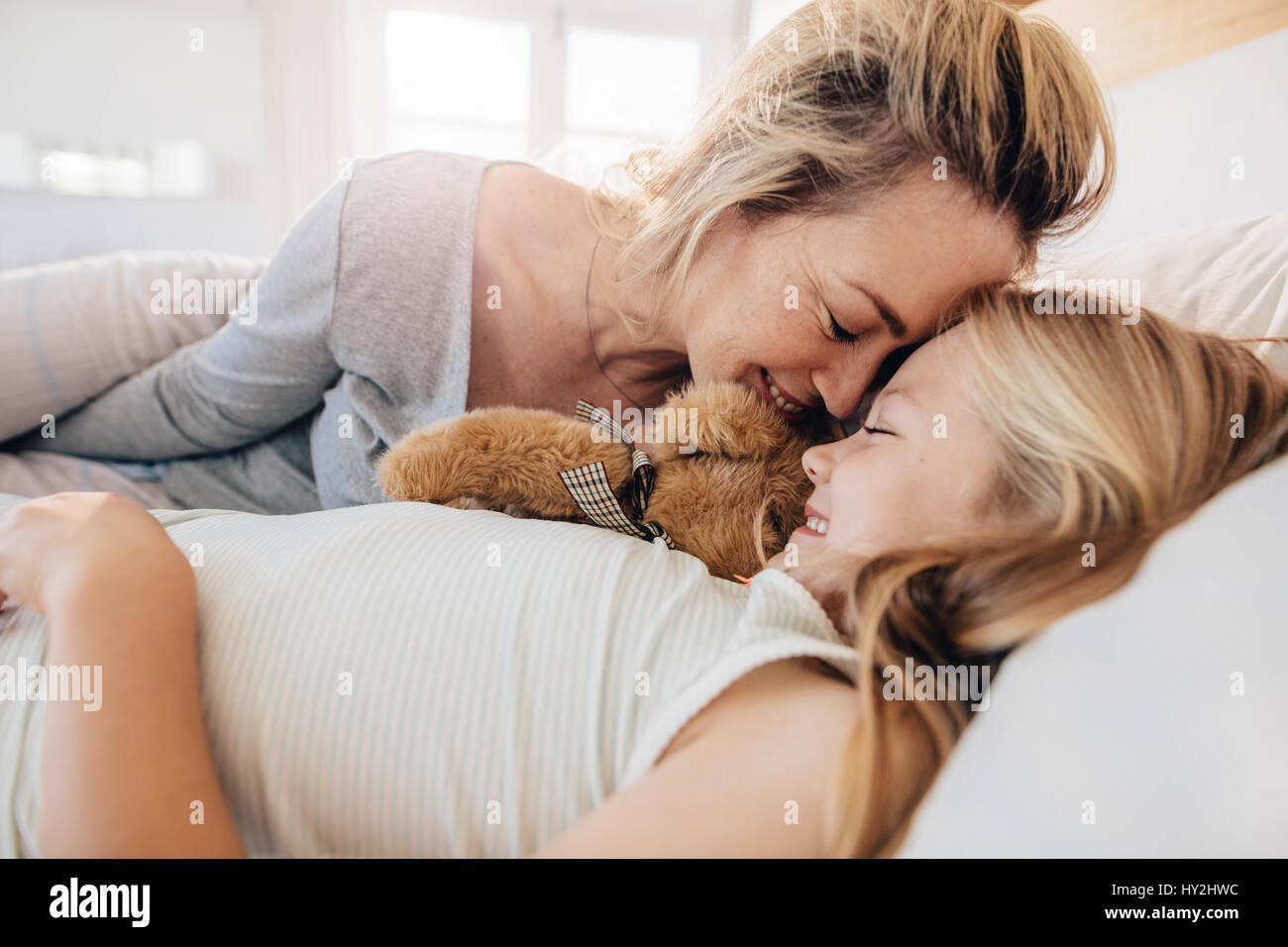 Cute little girl lying on bed with her mother. Mother and daughter sleeping together at home. Stock Photo