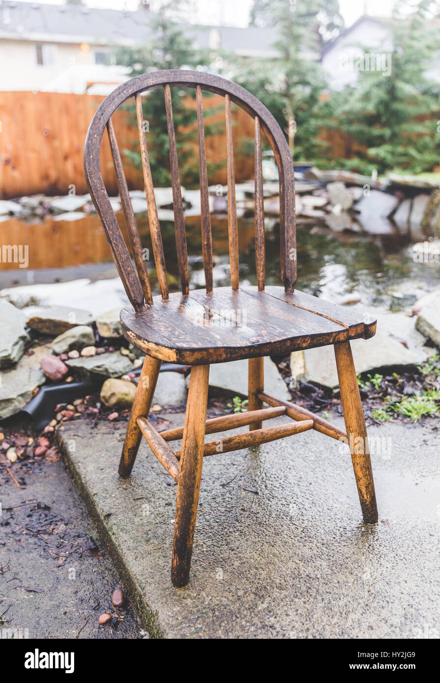 Antique, wooden chair in a home back yard near a pond in wet winter weather. Stock Photo