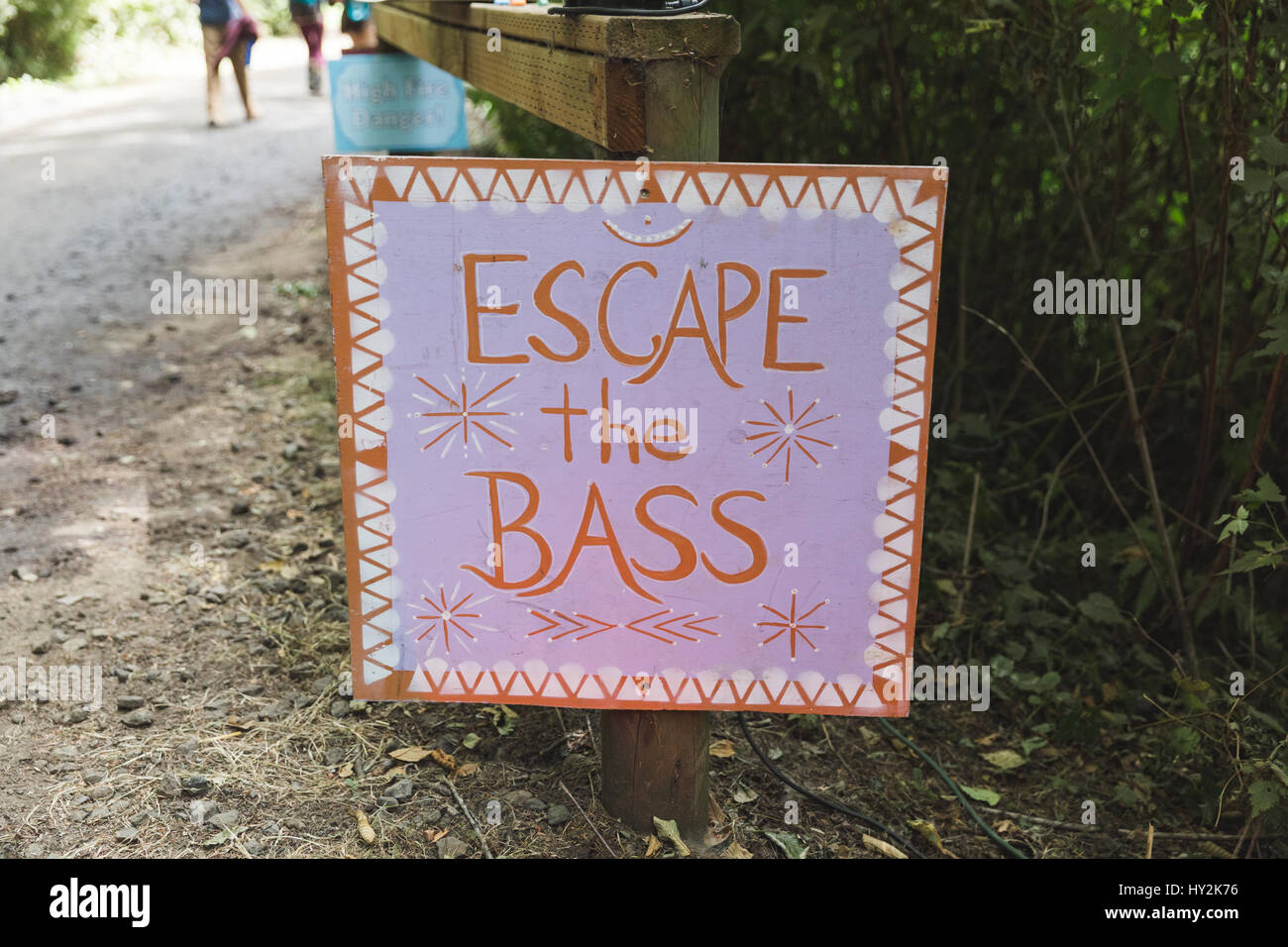 Sign reading 'Escape the BASS' posted on a path near the stage of an outdoor music festival. Stock Photo