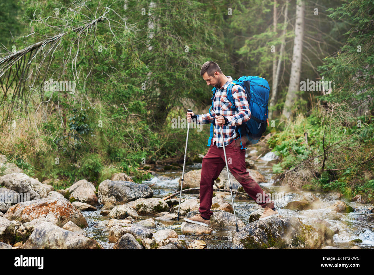 Hiker crossing a river in the forest Stock Photo