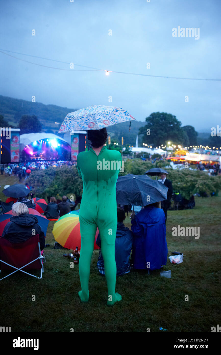 Man standing in a crowd wearing a green leotard with an umbrella watching live bands, The Green Man Festival, Wales. Stock Photo