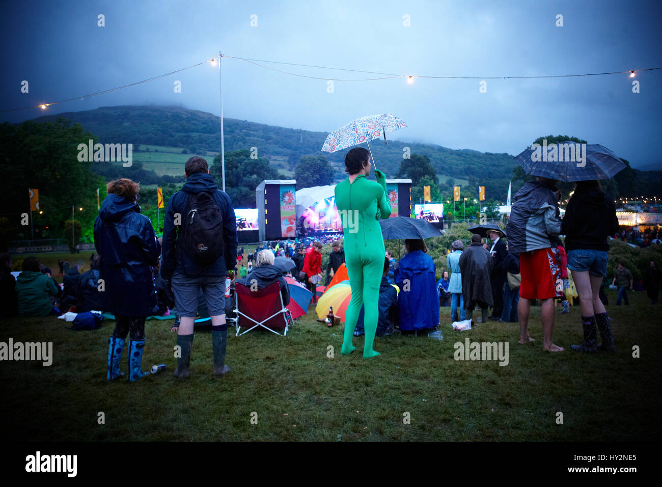 Man standing in a crowd wearing a green leotard with an umbrella watching live bands, The Green Man Festival, Wales. Stock Photo