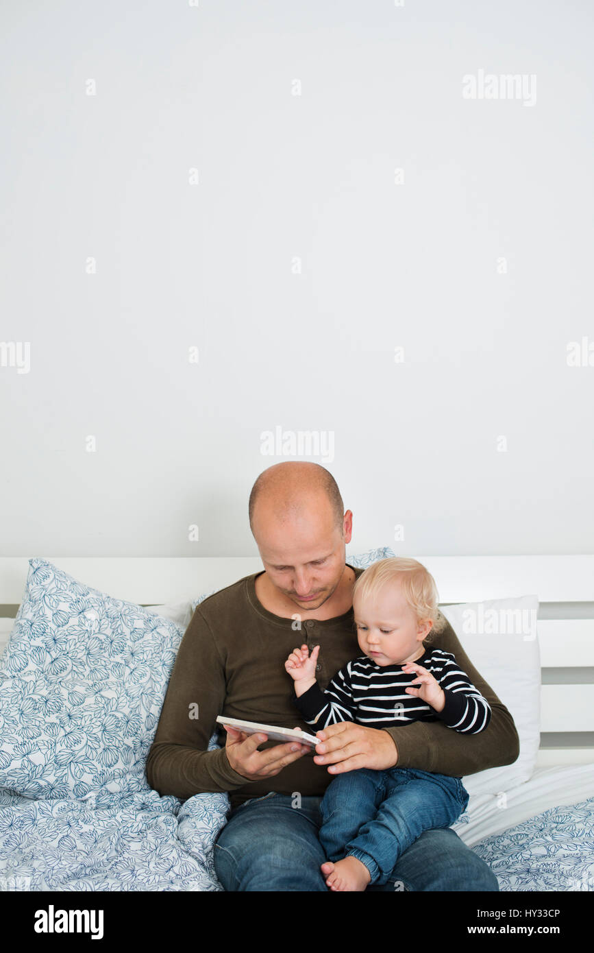 Sweden, Stay at home dad using tablet while holding son (12-17 months) Stock Photo