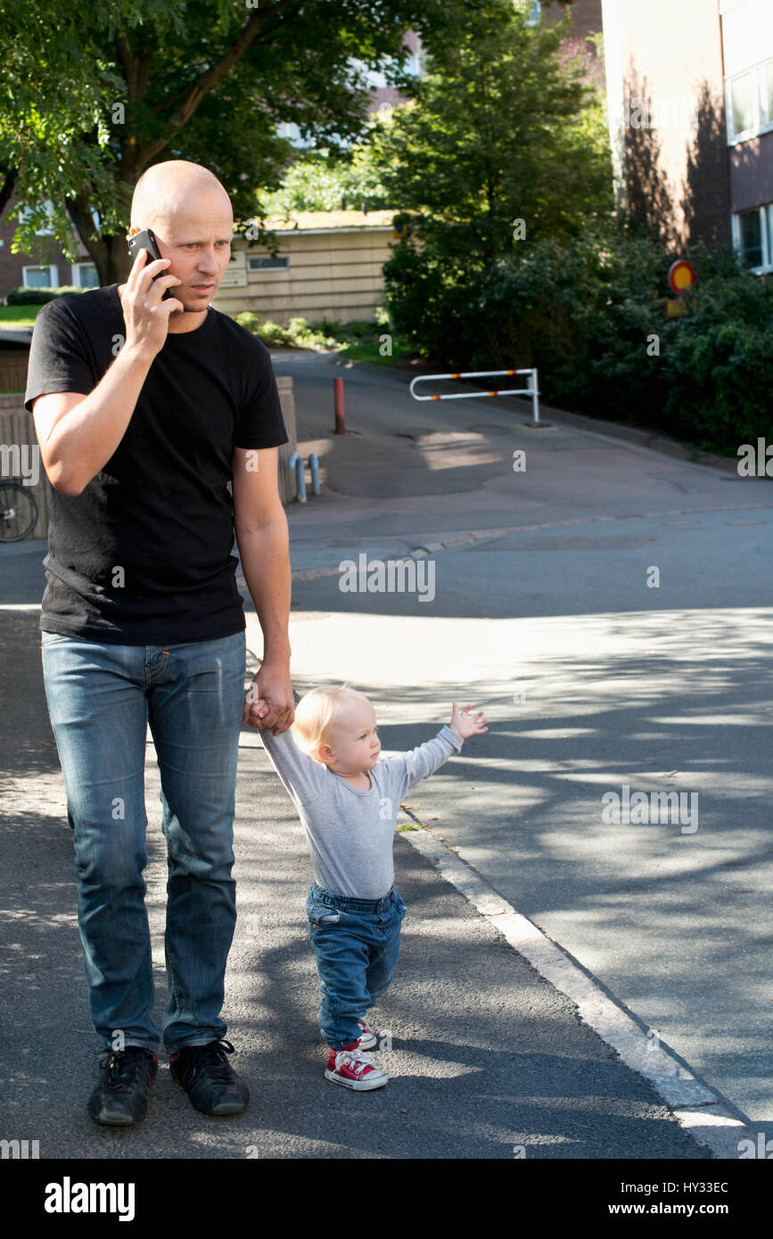 Sweden, Father and son (12-17 months) walking in city street Stock Photo