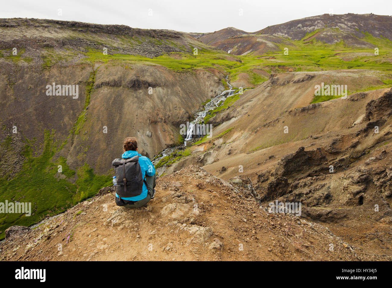 Iceland, Sudurland, Hveragerdi, Reykjadalur, Tourist looking at stream and waterfalls in rocky valley Stock Photo