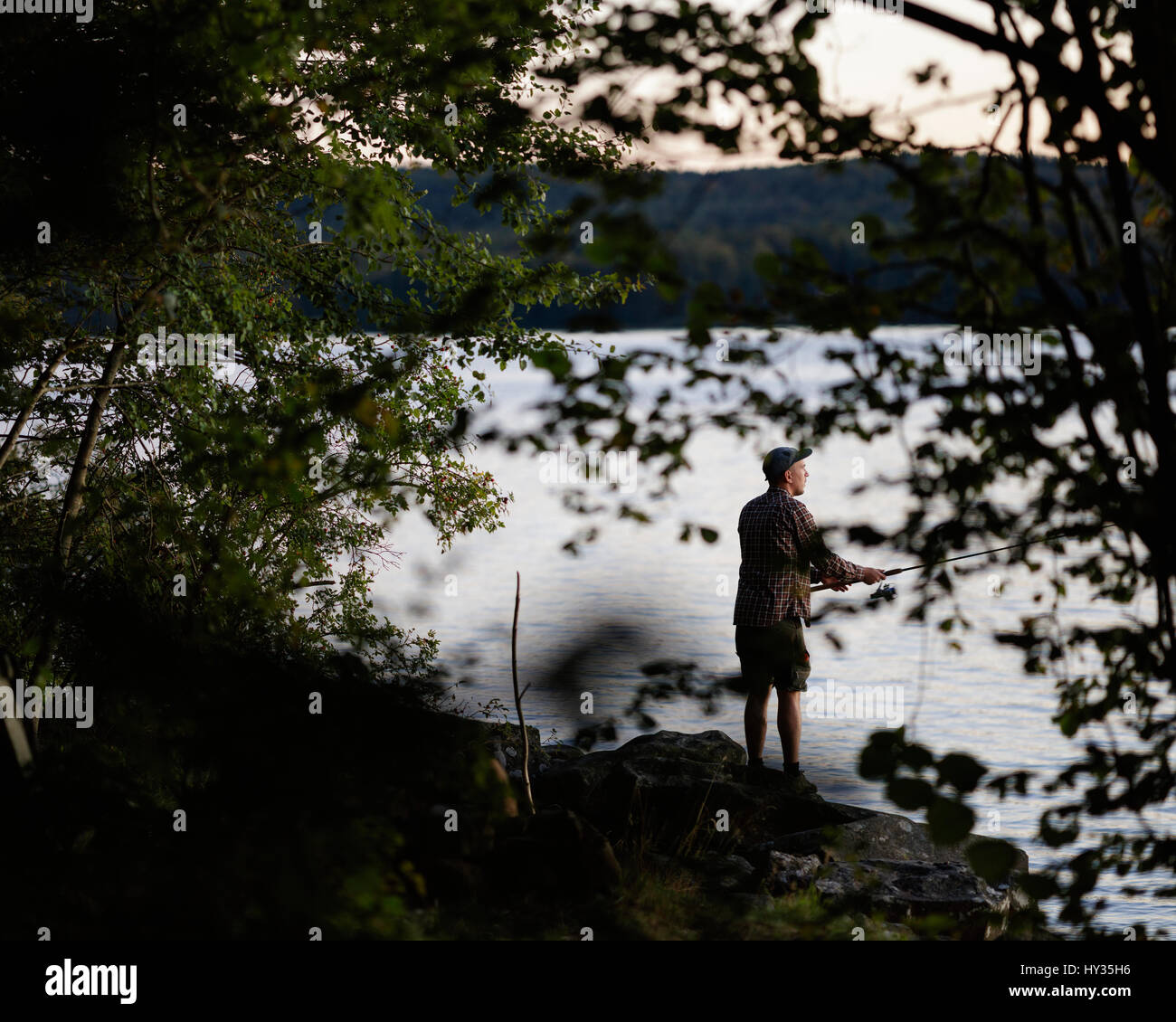 Sweden, Skane, Immeln, Man fishing in lake at sunset Stock Photo Alamy