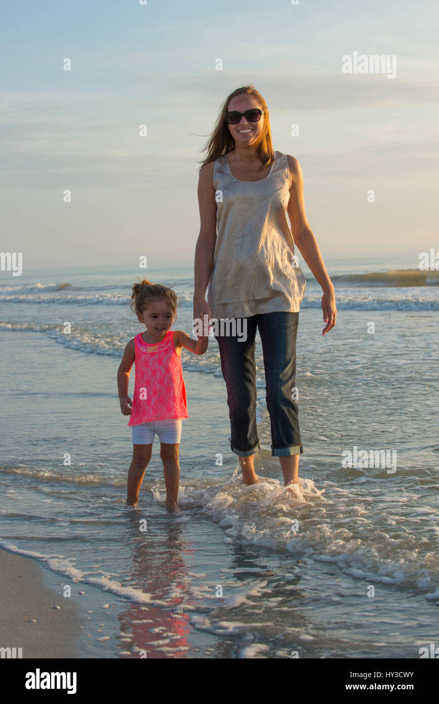 mom and daughter walking in the water at the beach smiling Stock Photo