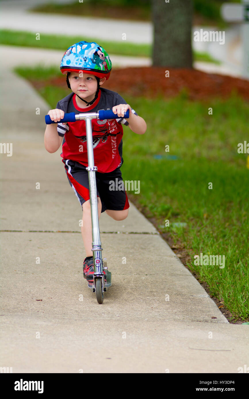 young boy riding scooter on sidewalk Stock Photo Alamy