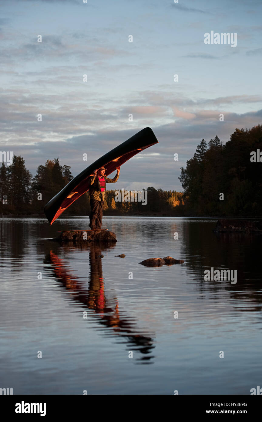 Sweden, Smaland, Man standing on stone in lake holding boat Stock Photo
