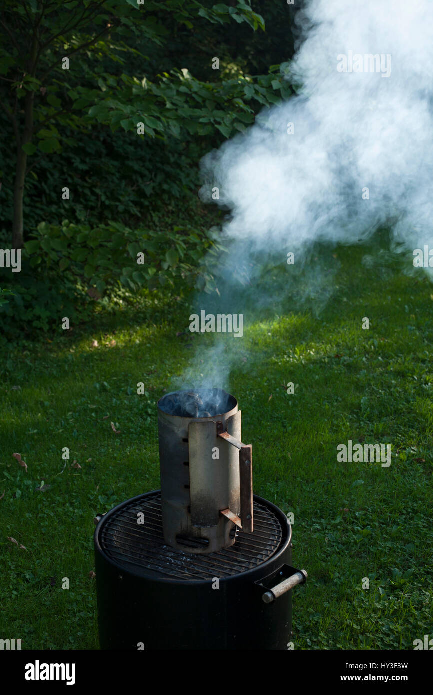 Charcoal chimney has started to smoke at backyard grill. Stock Photo