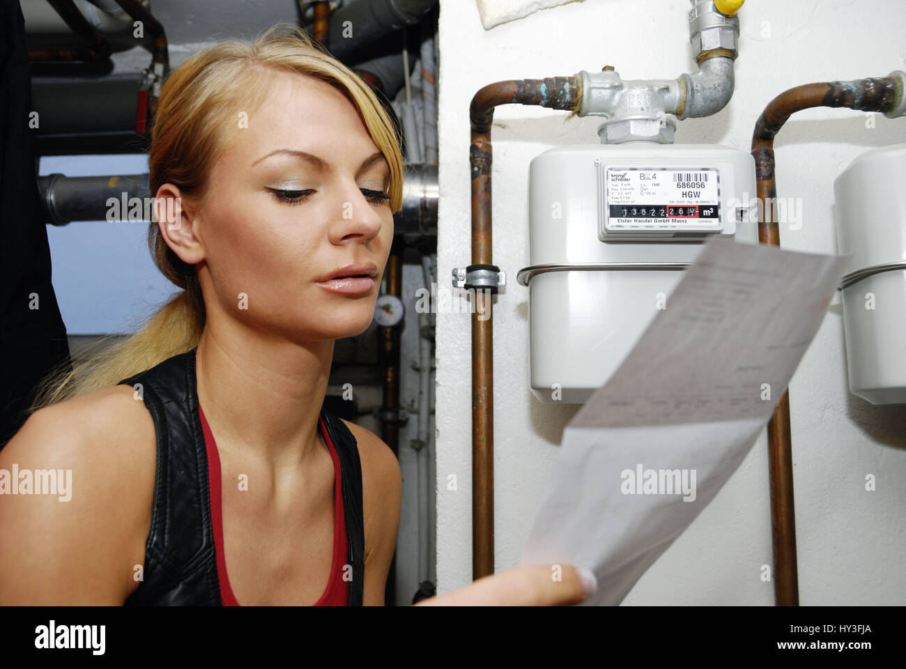 Young woman with heating costs account in the gas metre, Junge Frau mit Heizkostenabrechnung am Gaszähler Stock Photo