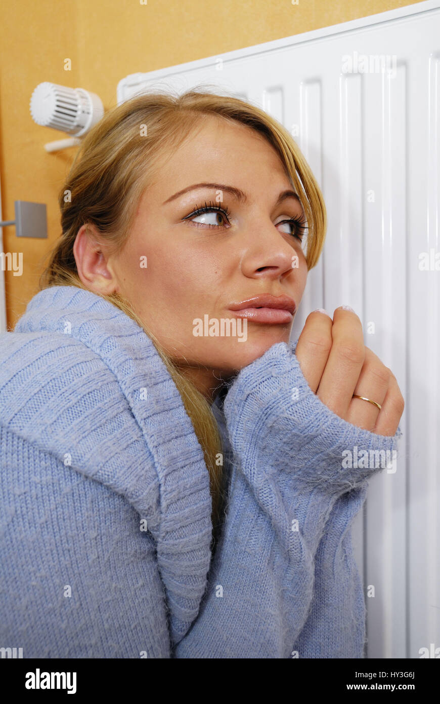 Young woman sits freezing before the heating, Junge Frau sitzt frierend vor der Heizung Stock Photo