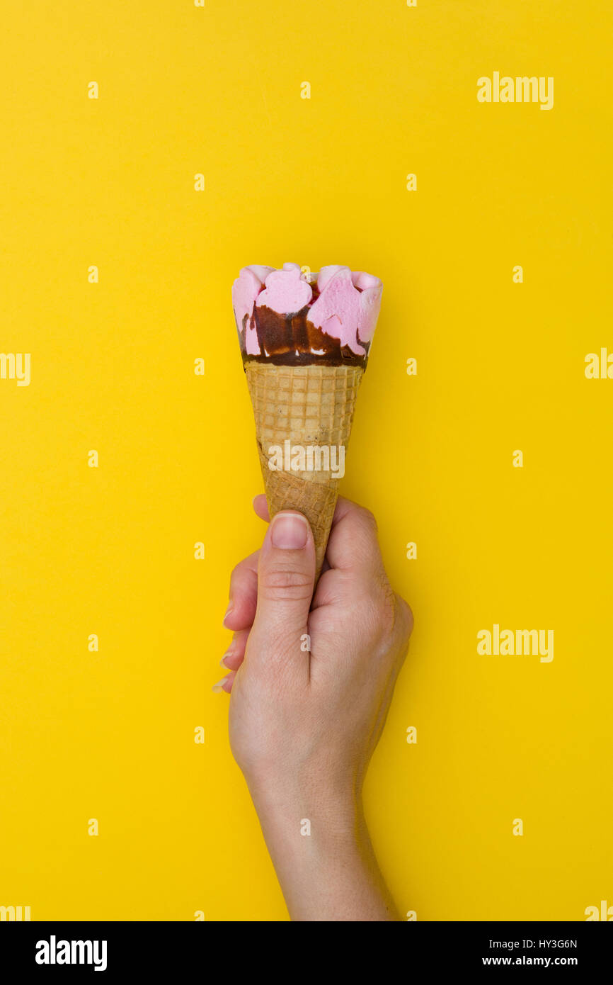 Hand holding ice cream cone on yellow background Stock Photo - Alamy