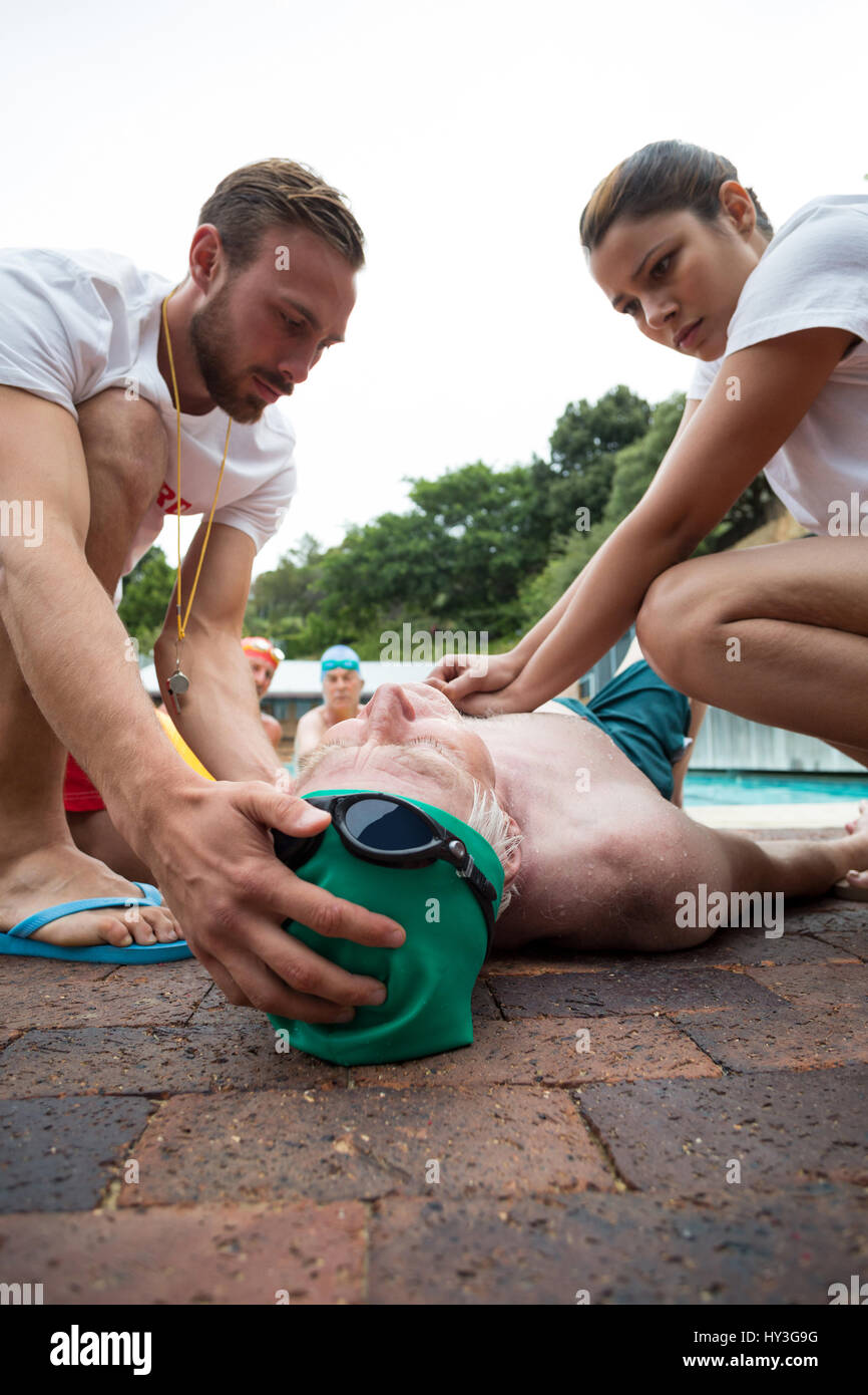 Male and female lifeguards pressing chest of unconscious senior man at poolside Stock Photo