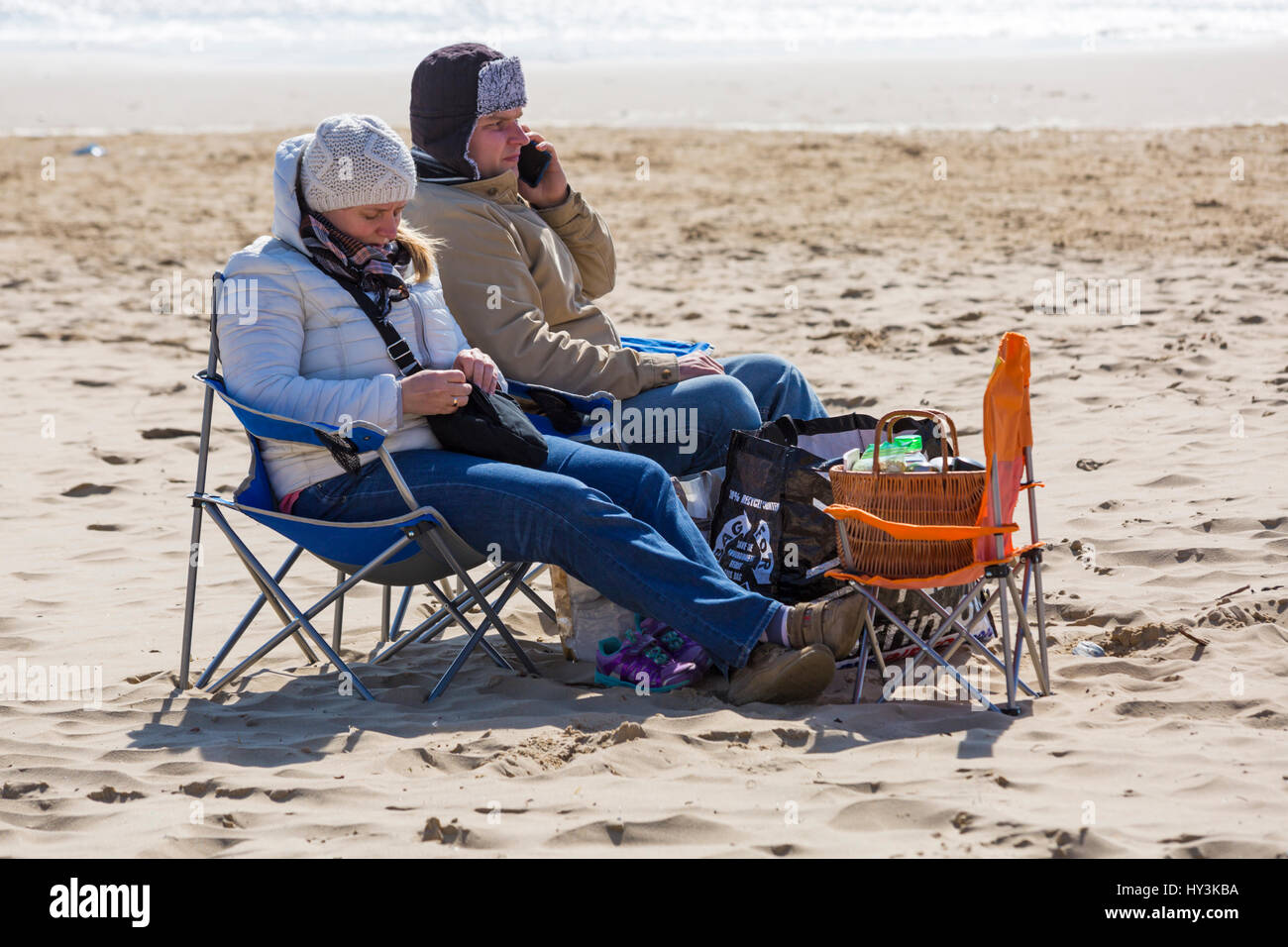 Bournemouth - couple sitting in seats wrapped up warm on Bournemouth beach in March Stock Photo