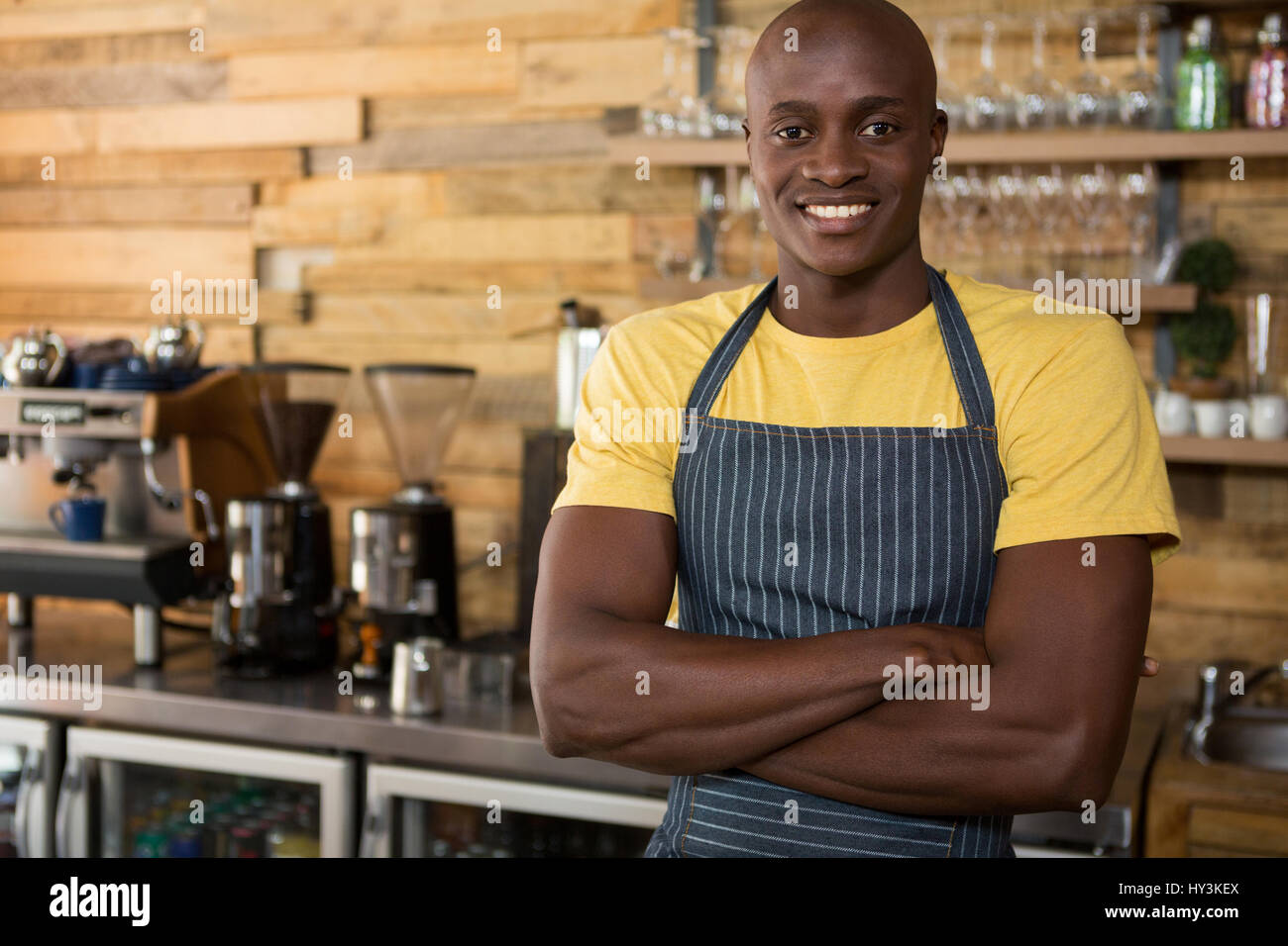Portrait of smiling male barista standing arms crossed in coffee shop