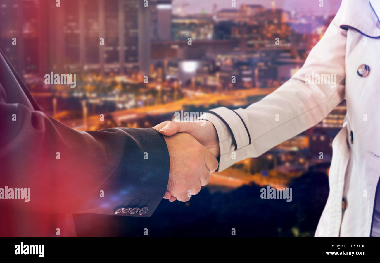 ale and female corporate people shaking hands against illuminated cityscape Stock Photo