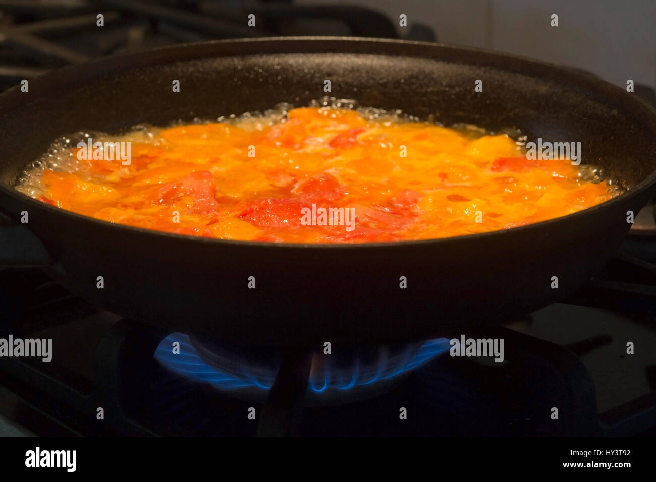 Red and yellow tomatoes cooking in cast iron frying pan over flame on
