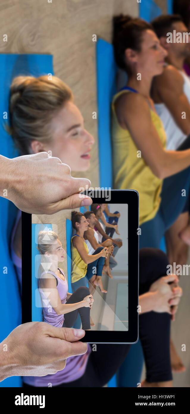 Cropped hand holding digital tablet against group of people doing leg flexes Stock Photo