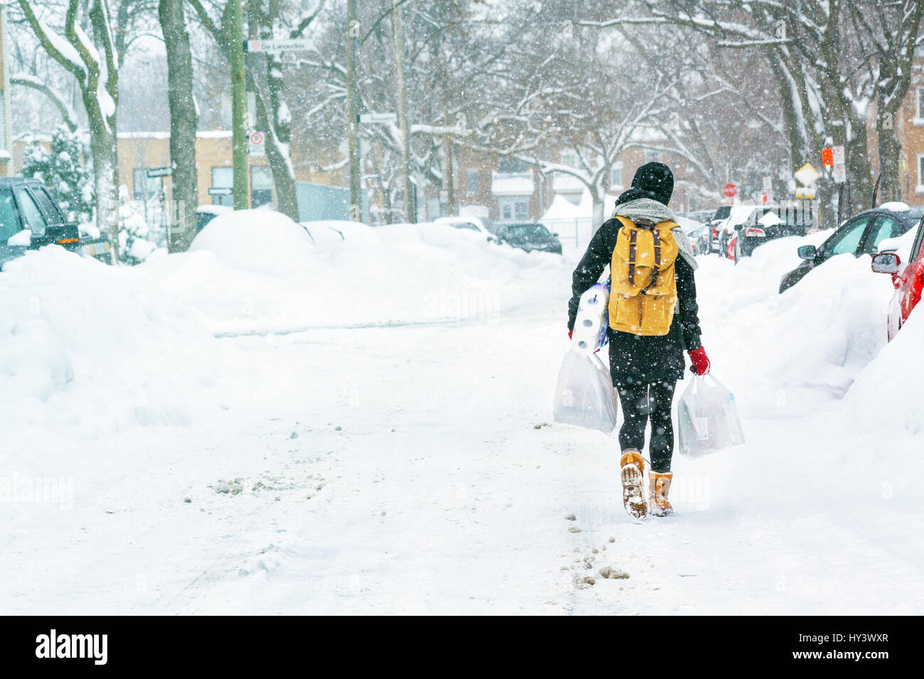 Person walking on snow with backpack and groceries bags. Stock Photo