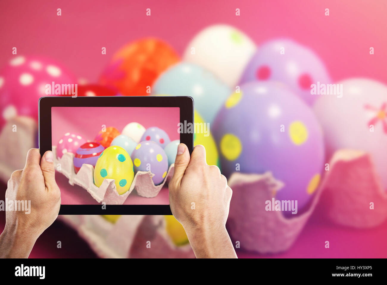 Cropped hand holding digital tablet against colorful easter eggs in egg carton Stock Photo