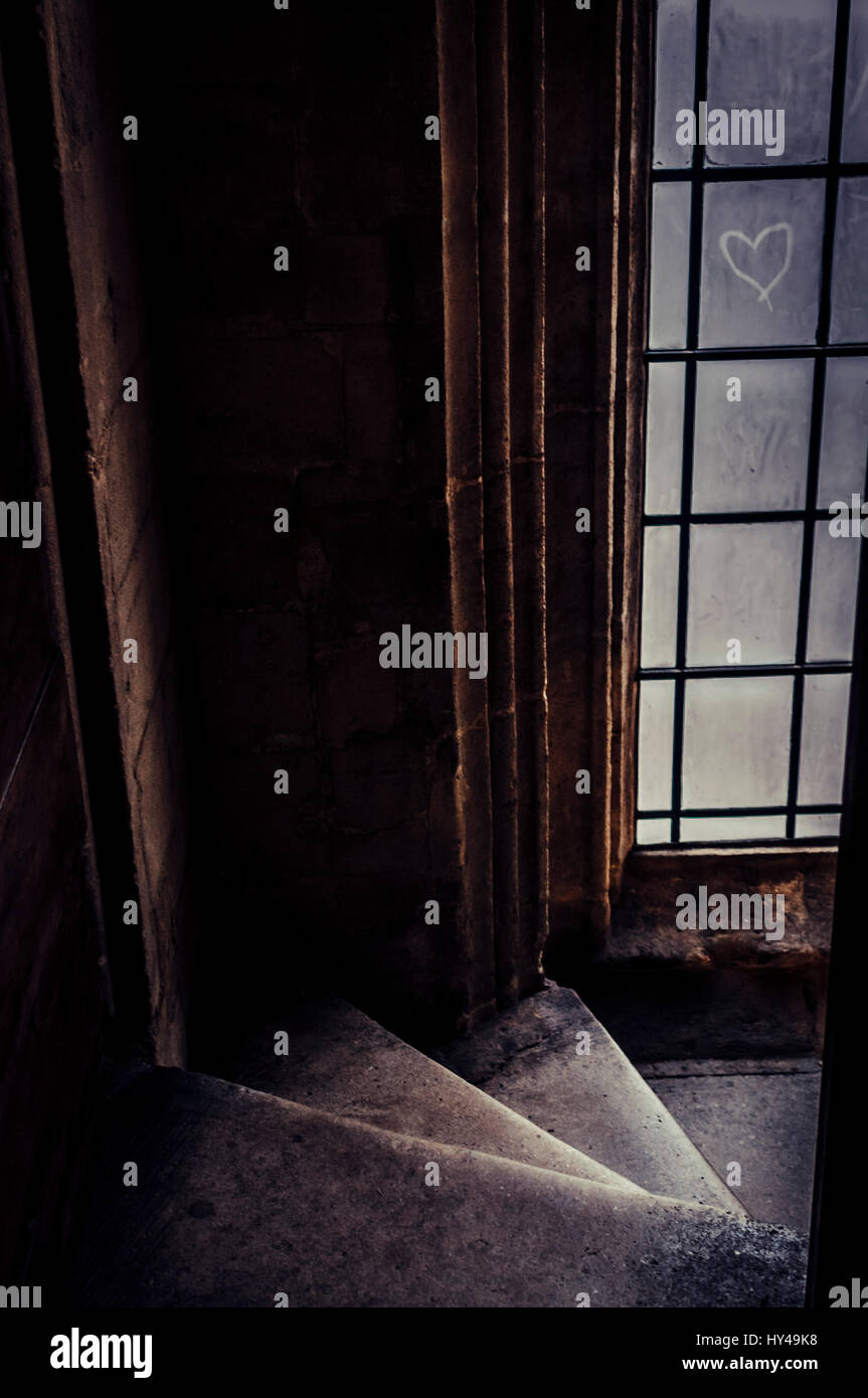 A colour photo of an eerie stairwell leading downwards with a dusty old window. A heart is drawn into the dust on the window pane. Stock Photo