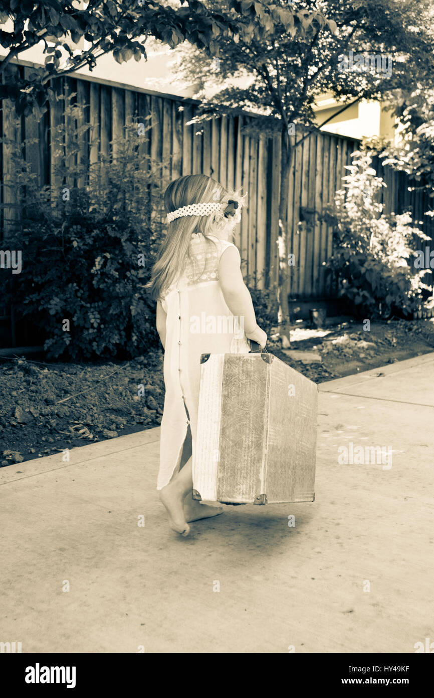 Little toddler girl with peasant lacey dress carrying luggage away as if she is a runaway. Stock Photo