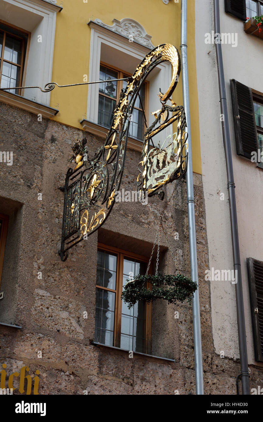 An advertising hanging sign of two men carrying grapes on a stick on the outside wall of a restaurant, Innsbruck, Austria Stock Photo