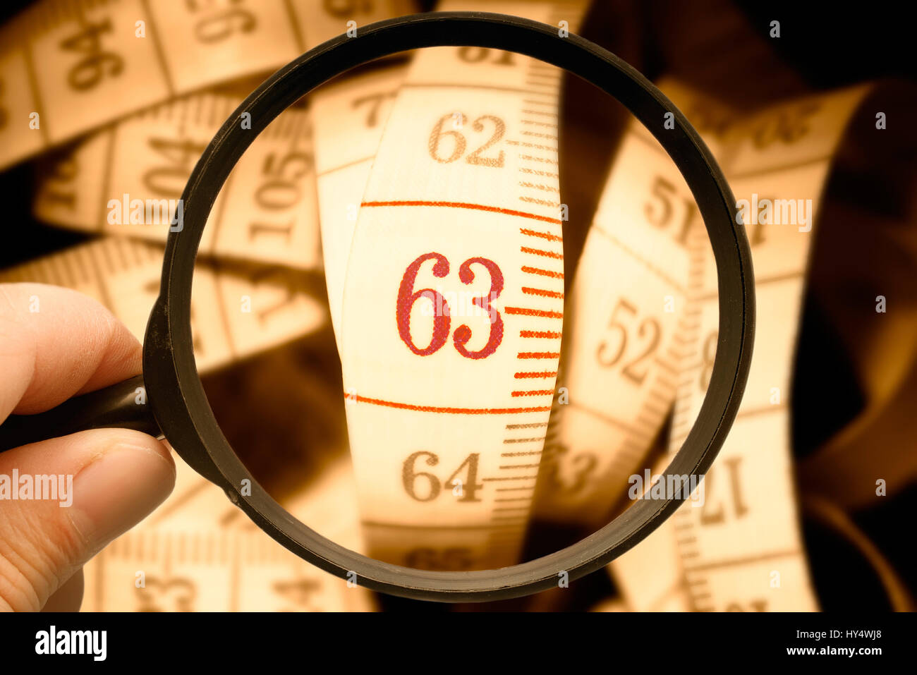 Dimension tape with the number 63 under the magnifying glass, symbolic photo pension with 63, Ma?band mit der Zahl 63 unter der Lupe, Symbolfoto Rente Stock Photo