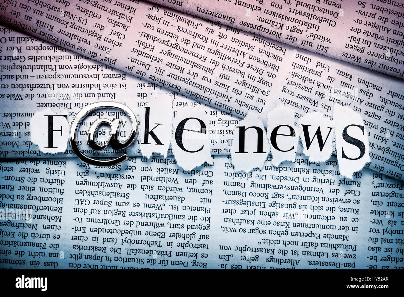 Stroke Fake news with at-sign on stacked newspapers, fake news on the Internet, Schriftzug Fake News mit At-Zeichen auf gestapelten Zeitungen, fake ne Stock Photo