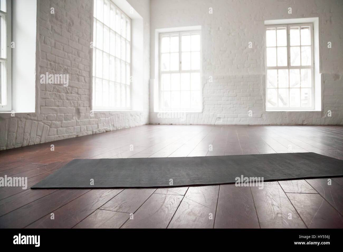 Empty white space in fitness center, white brick walls, natural wooden floor and big windows, modern loft studio, unrolled yoga mat on the floor, comf Stock Photo