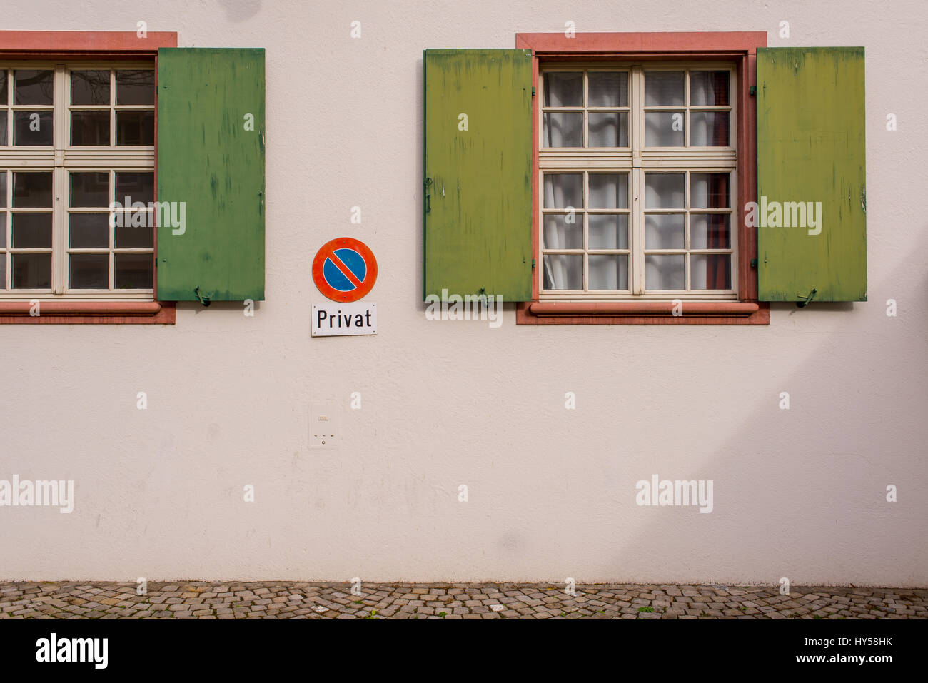 Wooden old medieval windows with green shutters on empty white wall with no parking sign and Privat (Private) written below Stock Photo