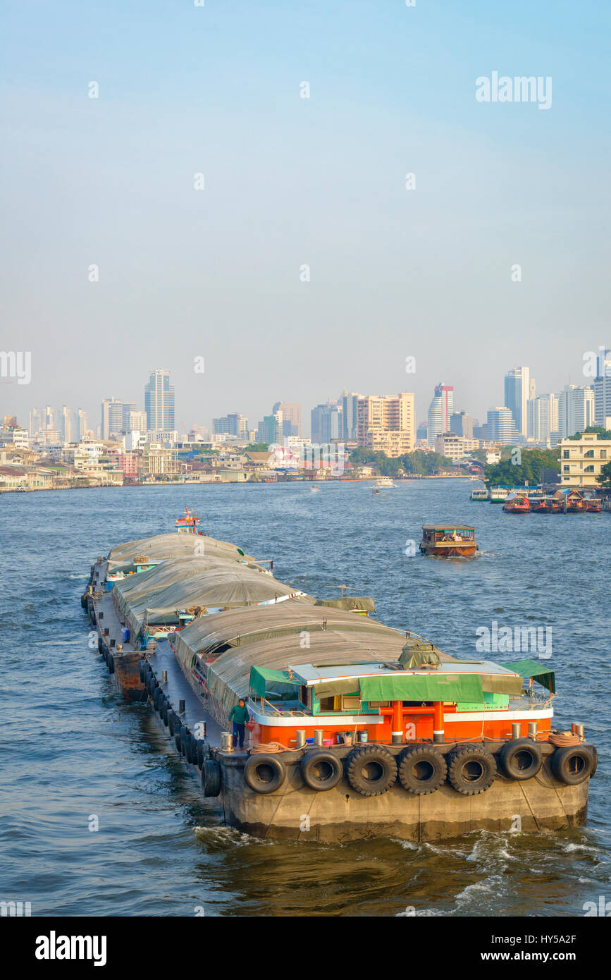 River transport in South East Asia: a cargo barge passes down the Chao Phraya River in Bangkok, Thailand, carriying freight, towed by a tug; goods Stock Photo