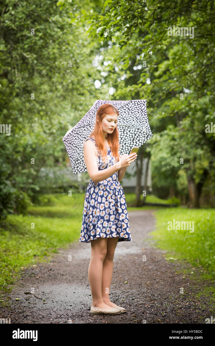 Finland, Pirkanmaa, Tampere, Woman wearing floral dress standing with umbrella in park Stock Photo