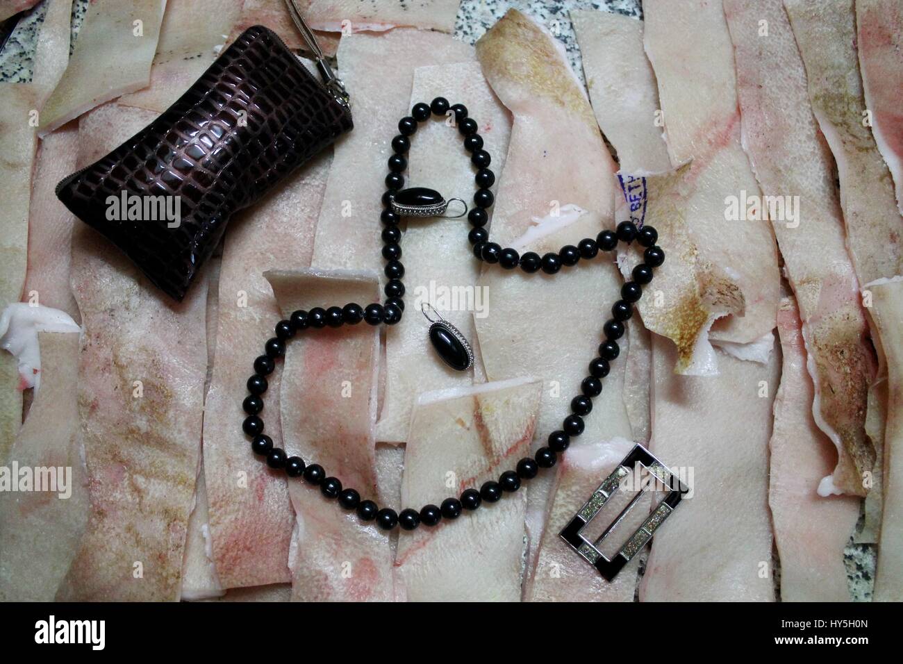 black beads with earrings and purse lay on pink fresh pork skin Stock Photo