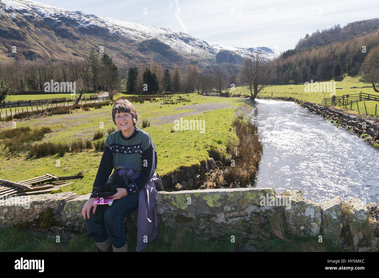Backlit scene of active retired woman in St John's in the Vale with snow capped Helvellyn in the background, Cumbria, England, UK Stock Photo