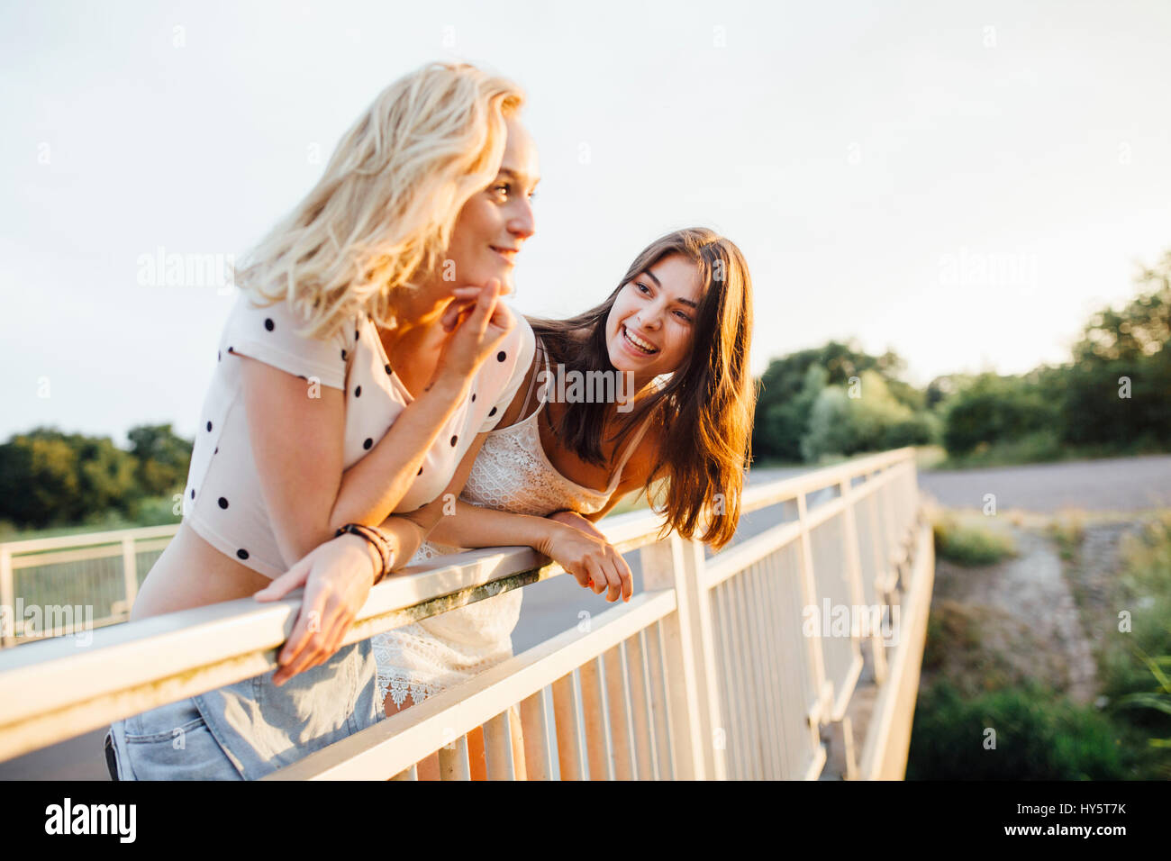 Two young women standing on a bridge, laughing and looking into the ...