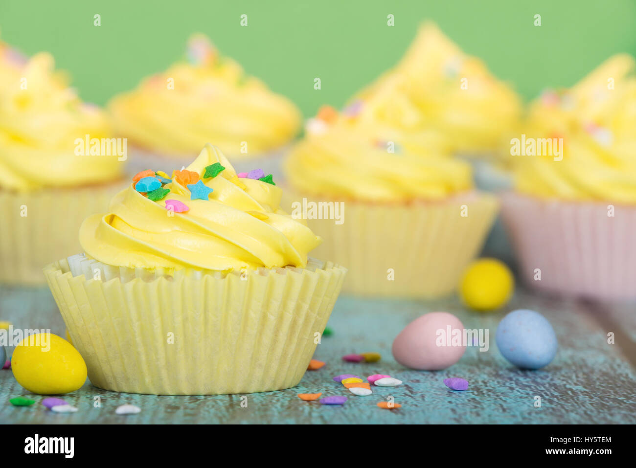Yellow Easter cupcakes with candy and sprinkles. Green background. Stock Photo