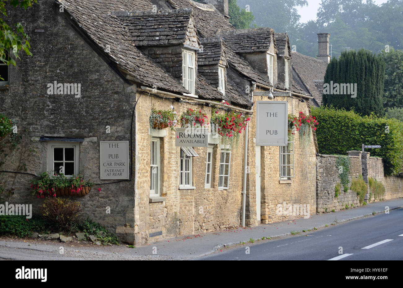 Old pub built out of Cotswold stone with stone tiles (slates) and hanging baskets in a town in the Cotswolds, England, UK. Stock Photo