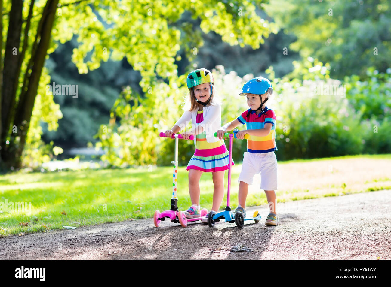 Children learn to ride scooter in a park on sunny summer day