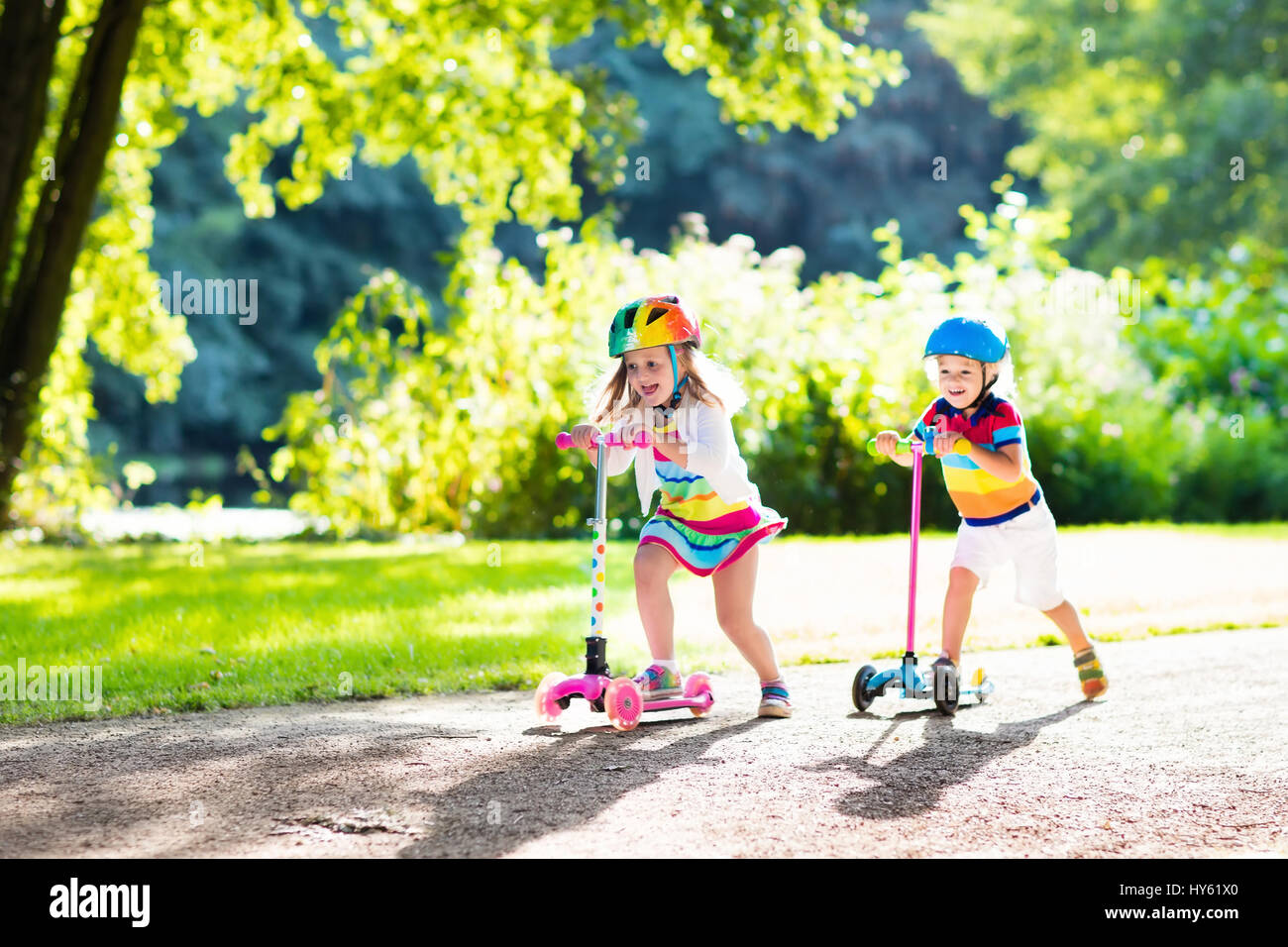 Children learn to ride scooter in a park on sunny summer day