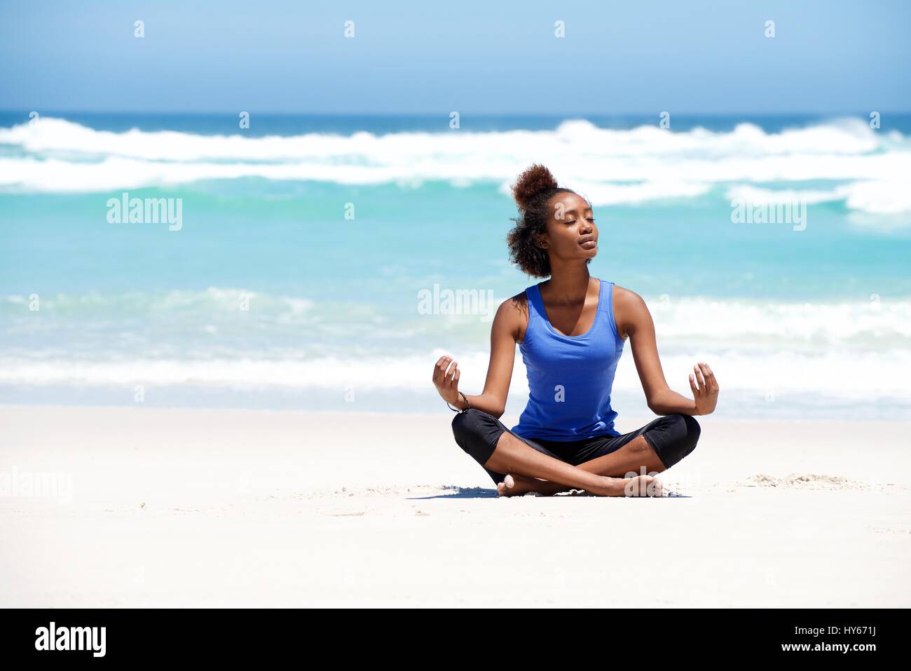 Portrait of healthy young yoga woman sitting in lotus pose at the beach ...